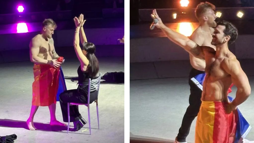 Doi artiști masculini fără tricou pe scenă interacționează cu o femeie din public, folosind un steag tricolor în timpul unui spectacol live