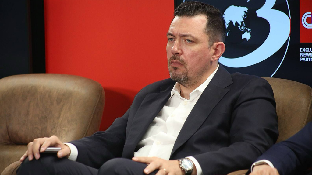 Alexandru Kansou participând la o conferință de business și tehnologie, îmbrăcat în costum elegant, într-un panel de discuții oficial.